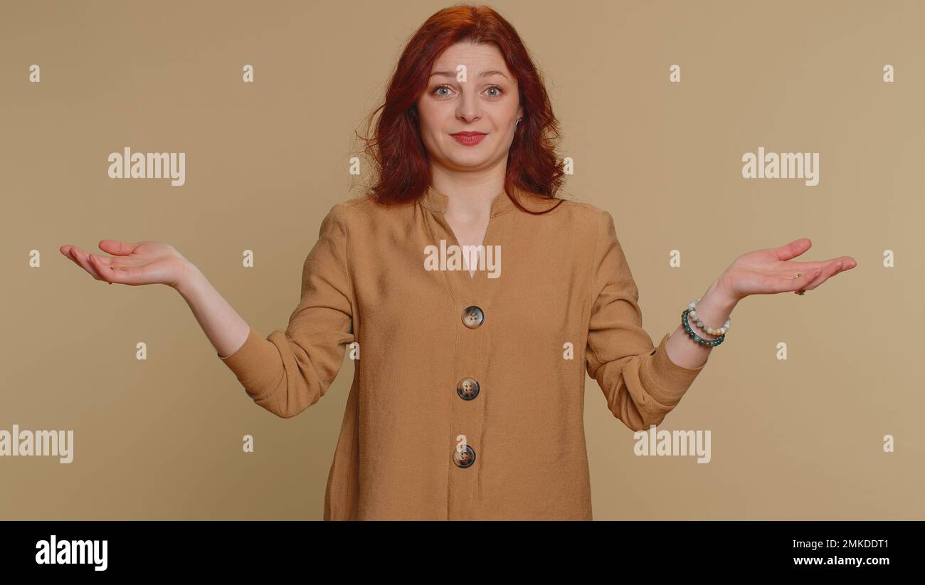 Je ne sais pas quoi dire. Femme confuse se sentant gênée par une question ambiguë, ayant des doutes, aucune idée, étant sans indice et incertaine. Jeune fille à tête rouge isolée sur fond de mur de studio beige Banque D'Images