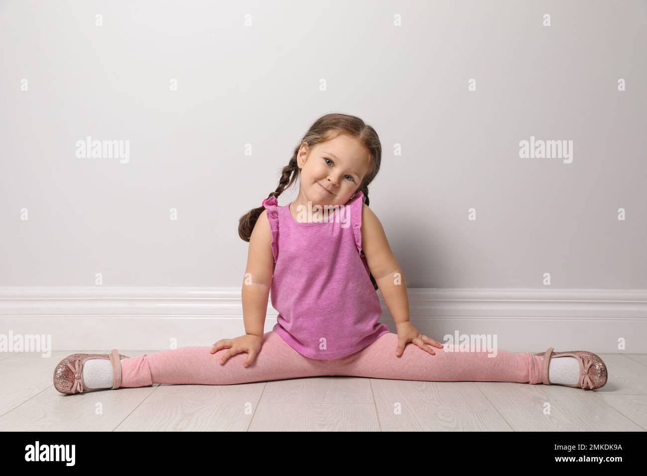 Petite fille mignonne sur le sol près du mur gris clair Banque D'Images