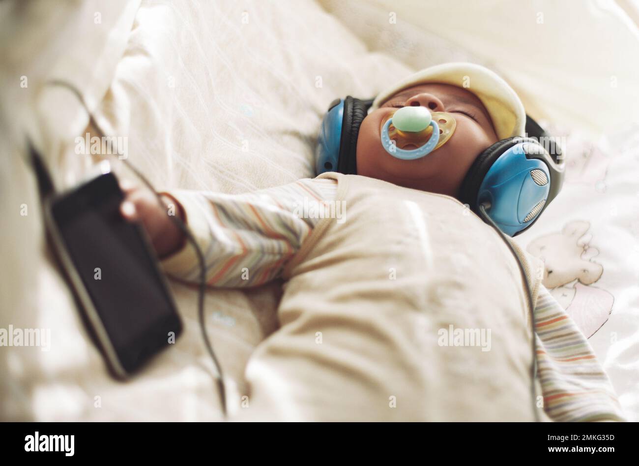 Un petit enfant dort dans un berceau et écoute de la musique dans de grands écouteurs Banque D'Images
