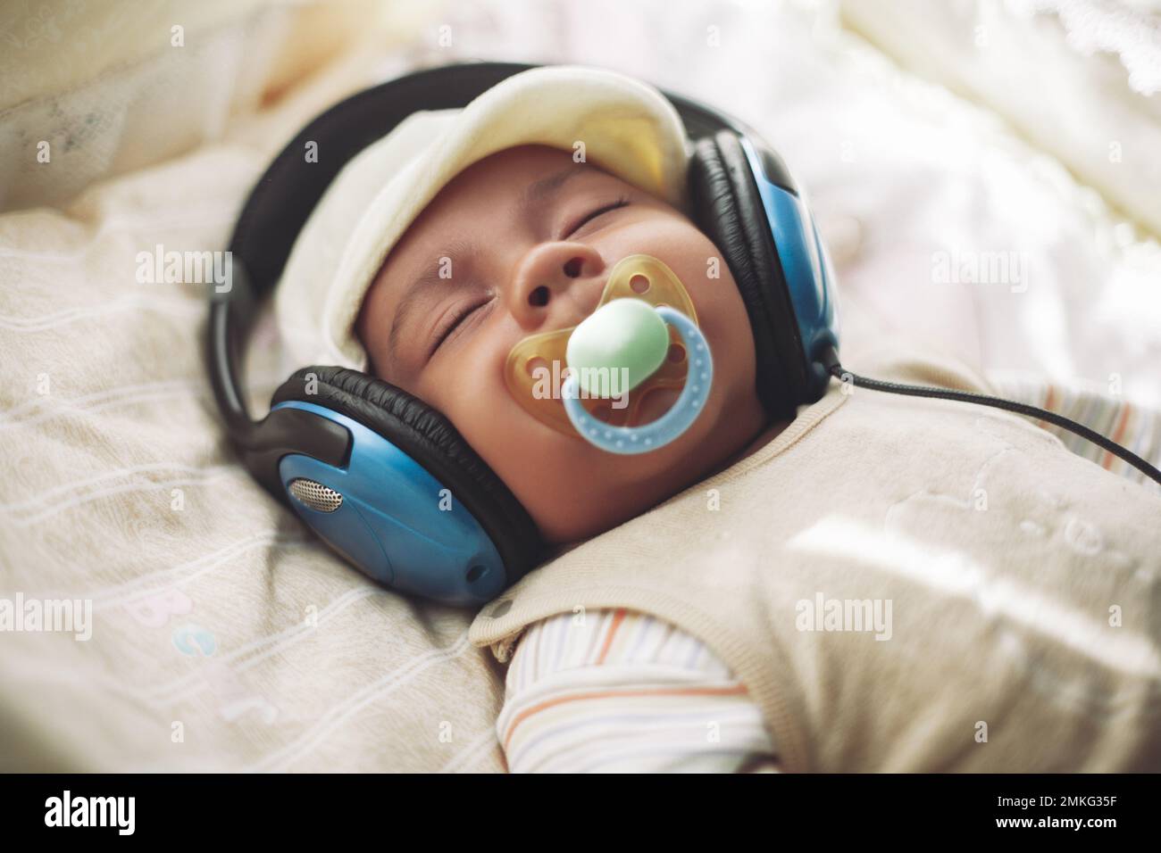 Un petit enfant dort dans un berceau et écoute de la musique dans de grands écouteurs Banque D'Images