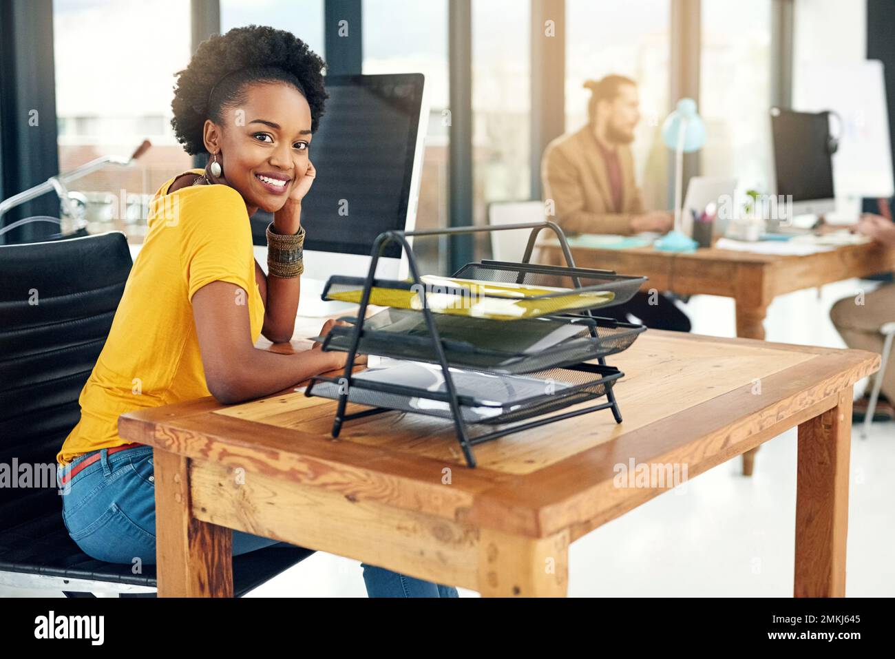 Je suis confiant quant à la réussite de cette entreprise. Portrait d'une jeune femme d'affaires assise dans un bureau avec des collègues en arrière-plan. Banque D'Images