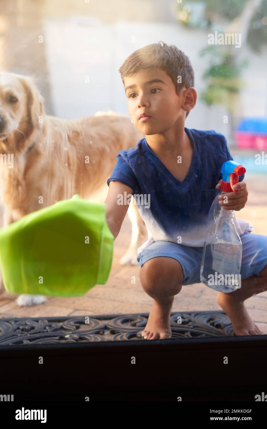 Maintenir les vitres propres et dégagées. un petit garçon lavant une porte en verre à la maison. Banque D'Images