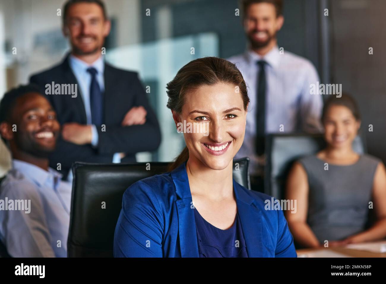 Remplissez votre journée avec des habitudes positives. Portrait d'une femme d'affaires souriante assise dans un bureau avec des collègues en arrière-plan. Banque D'Images