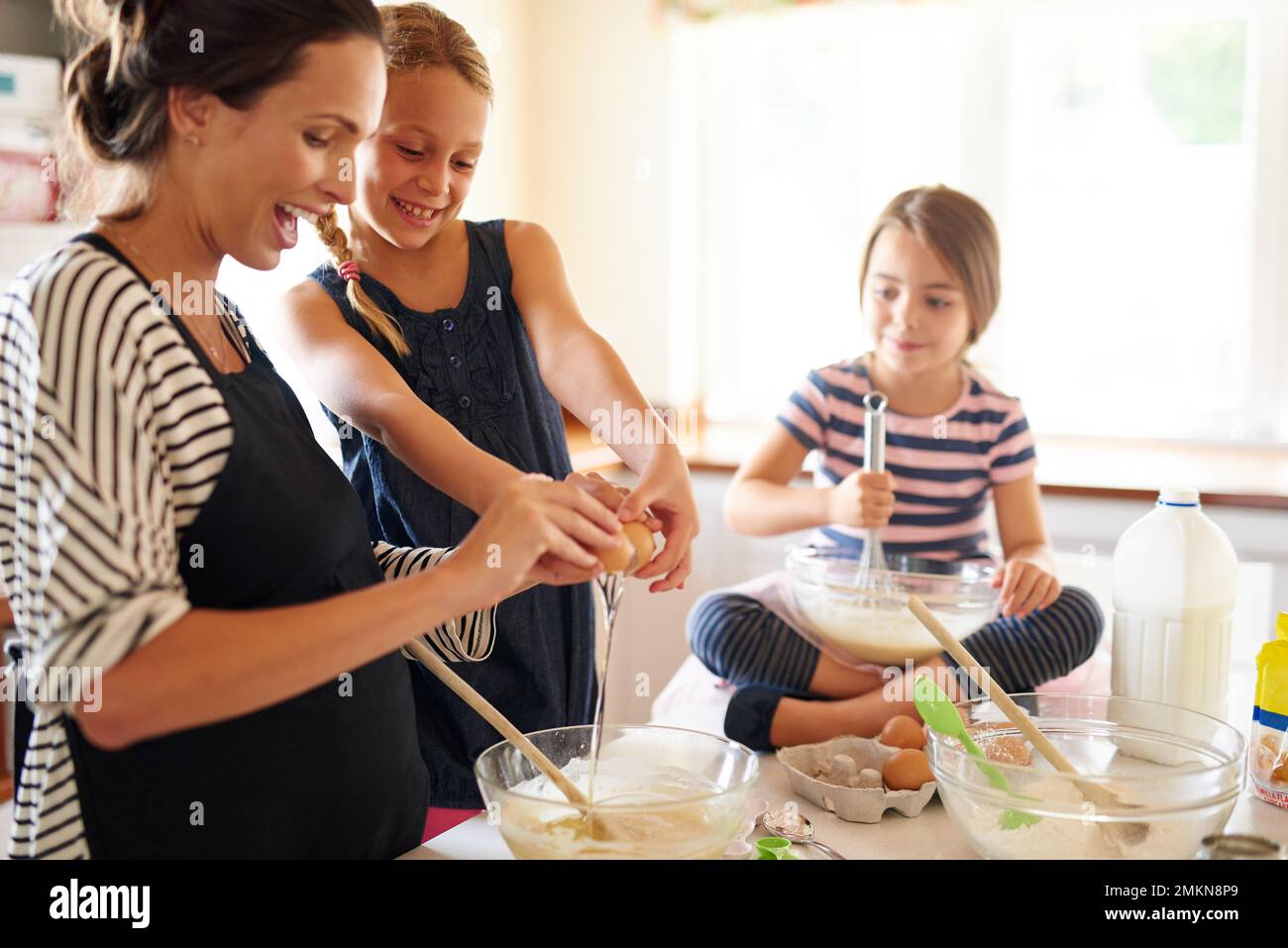 La pâtisserie est amusante pour toute la famille. deux petites filles qui cuisent avec leur mère dans la cuisine. Banque D'Images