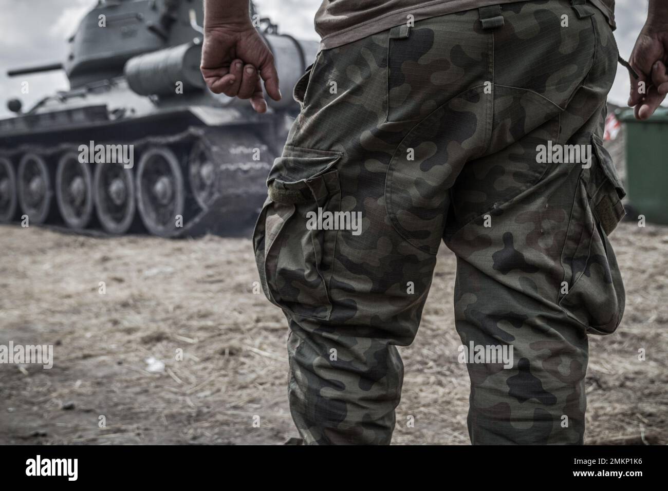 Des jambes de soldat sur un champ de bataille, portant un pantalon militaire de camouflage dans les bois, un pantalon de camouflage. Char de combat de l'armée en arrière-plan. Banque D'Images