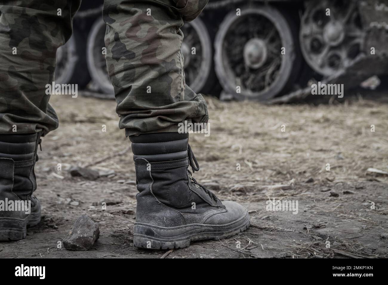 Des jambes de soldat sur un champ de bataille, portant un pantalon militaire de camouflage dans les bois, un pantalon de camouflage. Roues tracées de char d'armée en arrière-plan. Banque D'Images