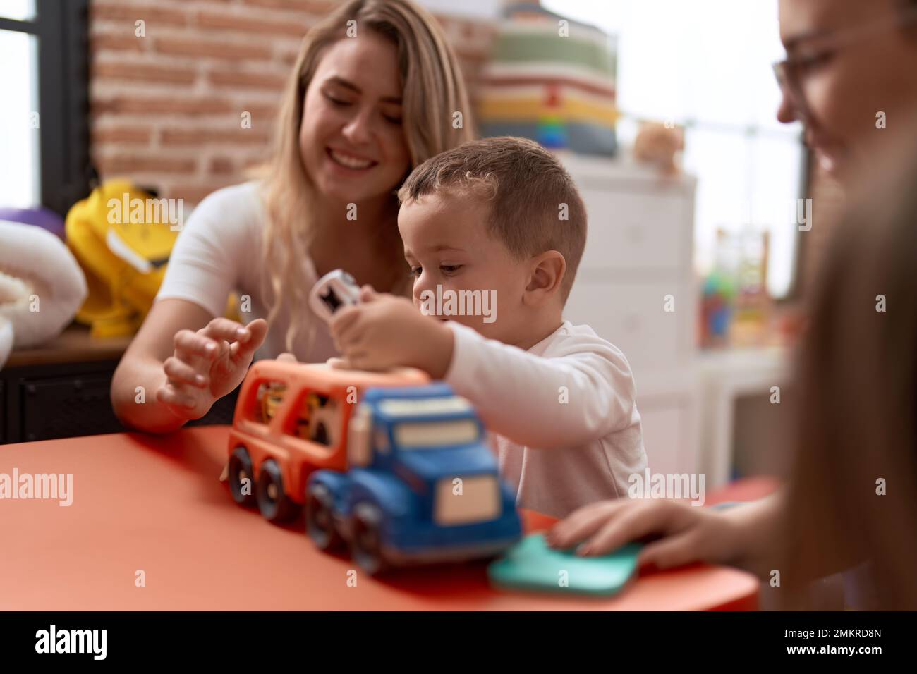 Enseignants avec un garçon et une fille jouant avec des voitures jouet assis sur une table à la maternelle Banque D'Images