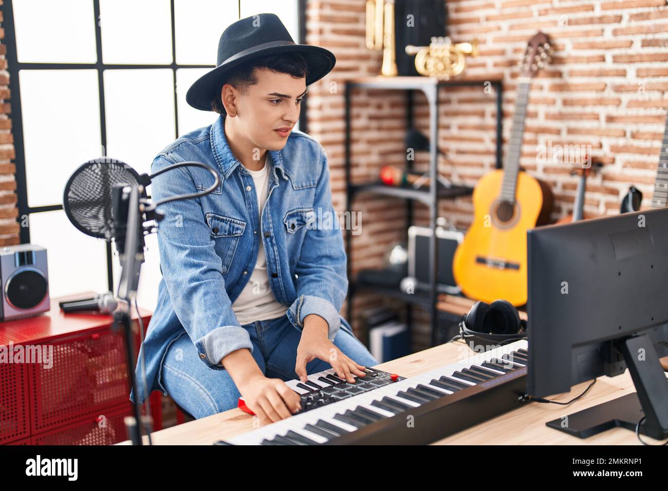 Jeune homme non binaire musicien jouant un clavier de piano dans un studio de musique Banque D'Images