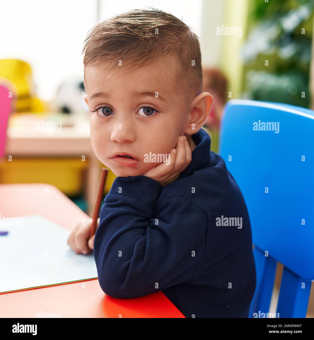 Adorable enfant hispanique, étudiant d'âge préscolaire, assis sur une table de dessin sur papier à la maternelle Banque D'Images