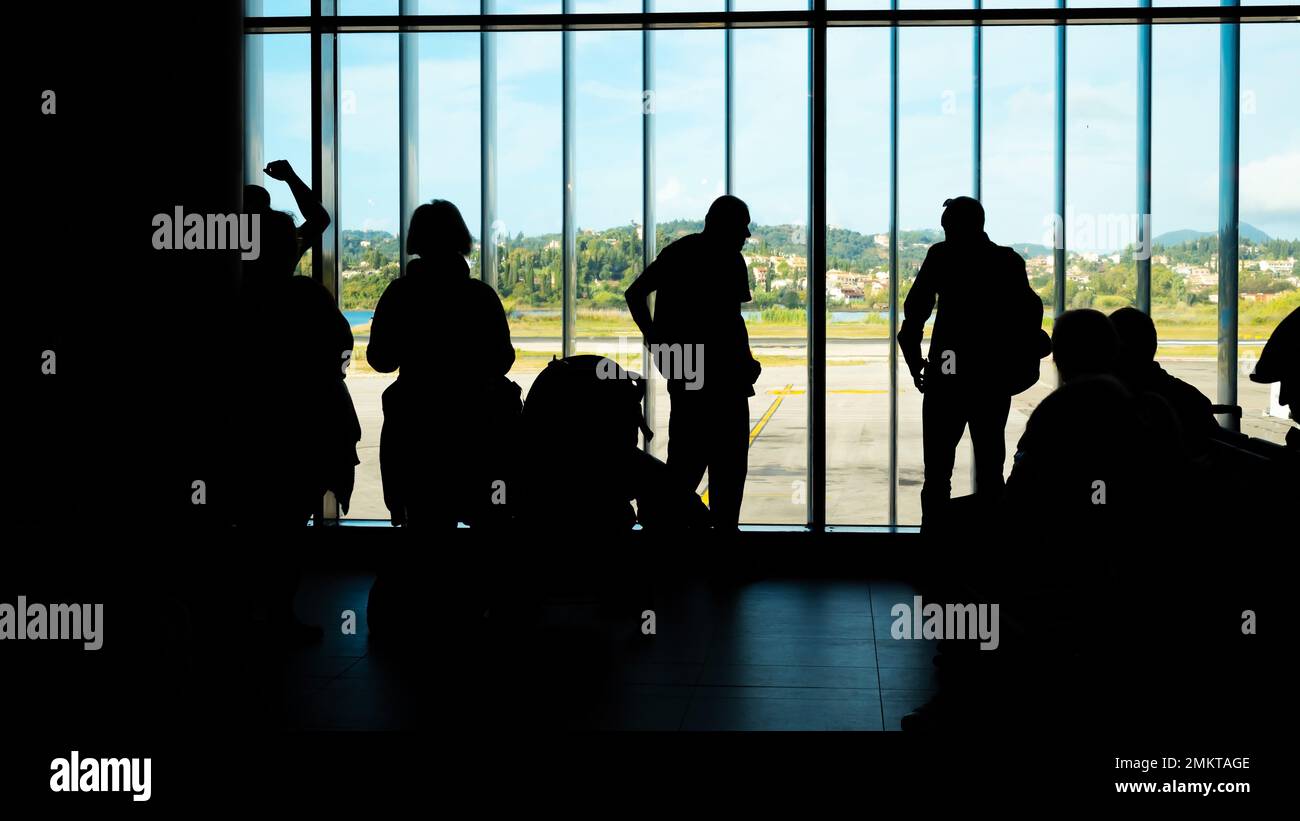 Kerkyra, Grèce - 09 29 2022: Silhouettes de personnes avec des bagages à main et billets d'entrée en attente de départ de leur avion dans le salon de l'aéroport. Banque D'Images