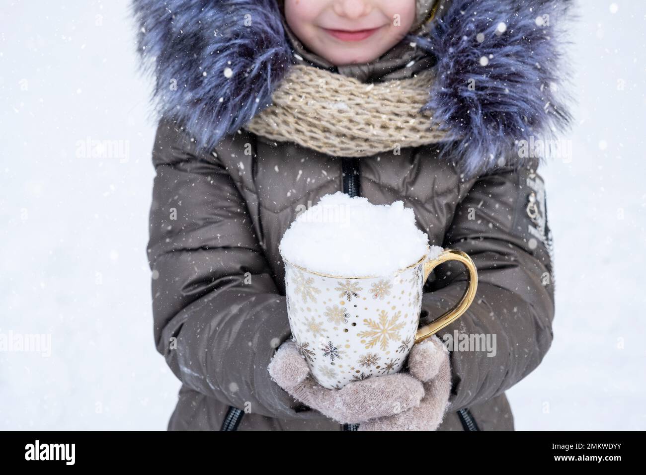 Une fille en vêtements chauds d'hiver pour l'extérieur tient une tasse avec de la neige dans ses mains - temps froid, saisonnalité. Noël et nouvel an Banque D'Images