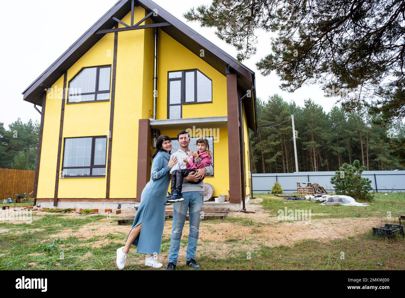 Famille heureuse dans la cour d'une maison inachevée - achat d'un chalet, hypothèque, prêt, relocalisation, construction Banque D'Images