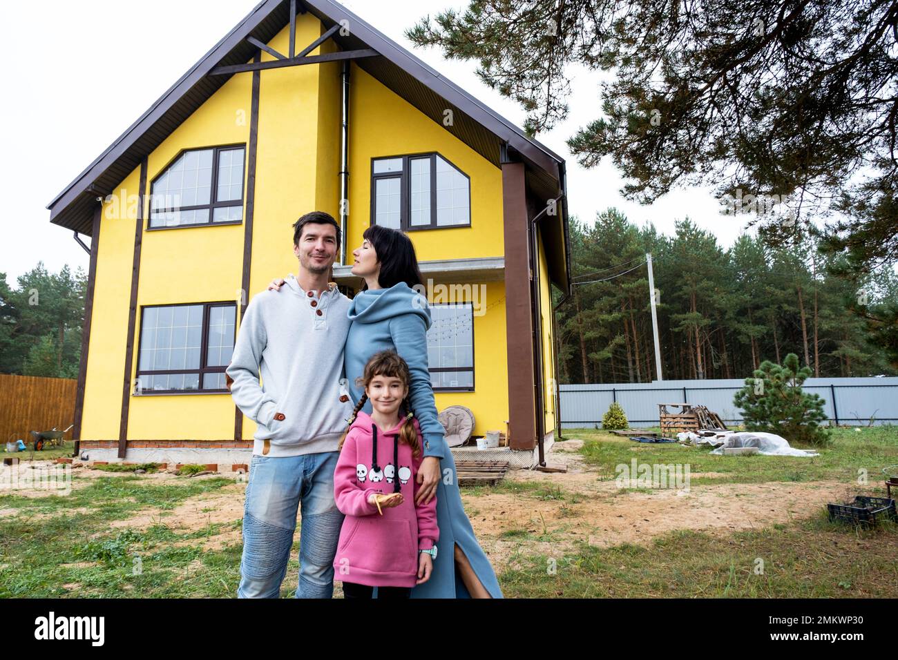 Famille heureuse dans la cour d'une maison inachevée - achat d'un chalet, hypothèque, prêt, relocalisation, construction Banque D'Images