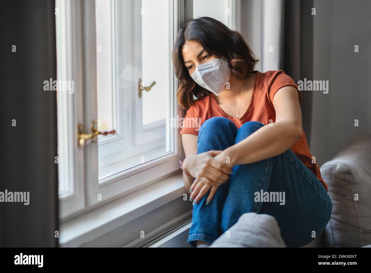 Jeune femme arabe déprimé portant un masque de protection assis près du vent à la maison Banque D'Images