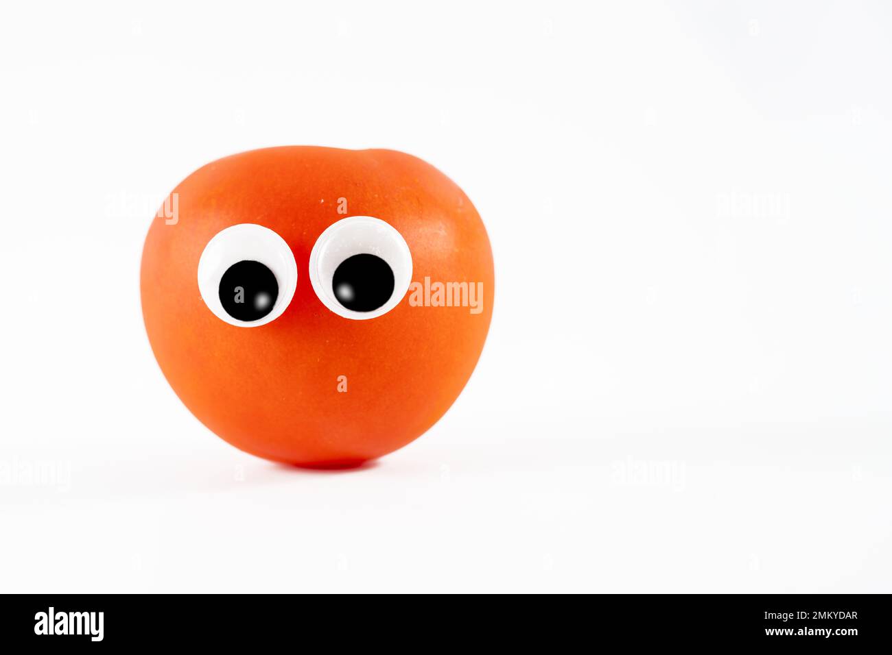 grande tomate mûri au soleil avec des yeux de dessin animé roulant googly isolés sur fond blanc Banque D'Images