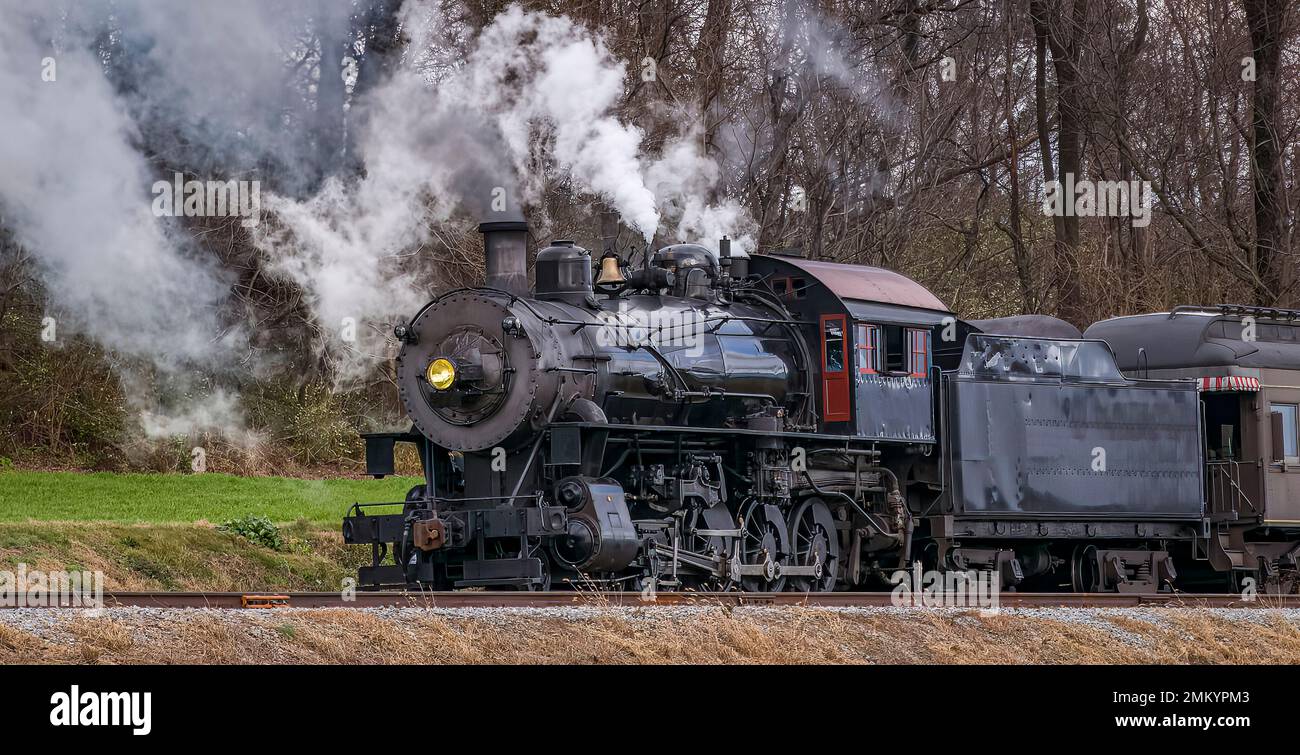 Vue sur un train de voyageurs à vapeur classique, qui dégage beaucoup de fumée et de vapeur, tout en voyageant à la campagne le jour de l'automne Banque D'Images