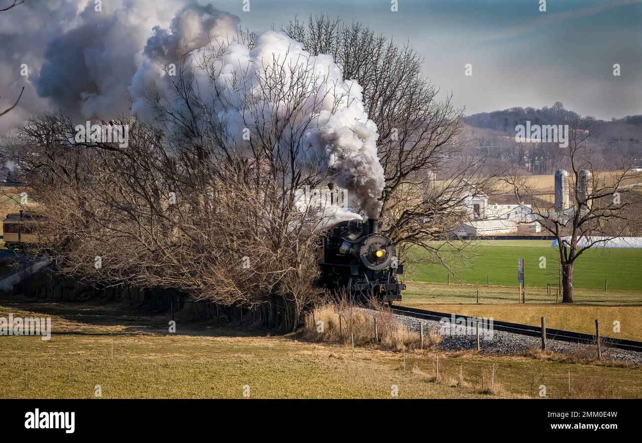 Vue sur un train de passagers à vapeur classique qui s'approche, qui se déplace à travers la campagne, qui dégage de la fumée et de la vapeur lors d'une journée d'hiver Banque D'Images