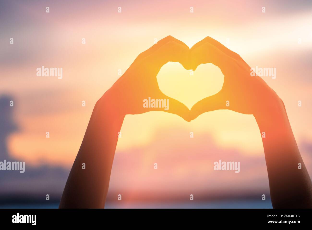 Mains formant un coeur avec silhouette de coucher de soleil Banque D'Images