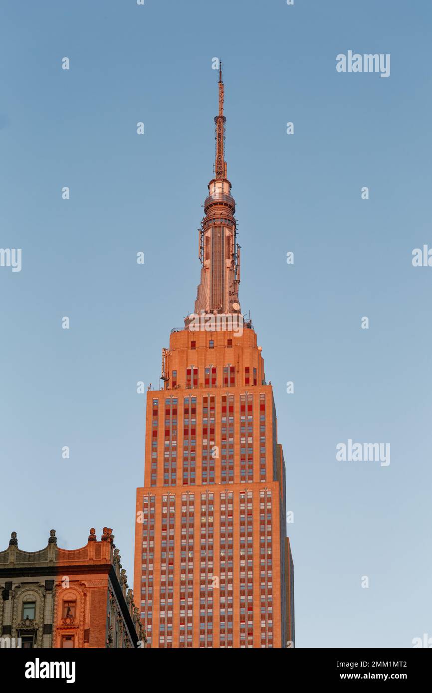 NYC : la façade est de l'Empire State Building passe du gris au rouge doré à l'aube, lorsque le soleil est à son point le plus bas. Banque D'Images