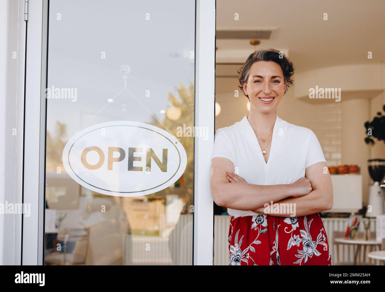 Propriétaire de café réussi souriant à la caméra tout en se tenant à côté d'un panneau ouvert à la porte de son restaurant. Femme propriétaire de petite entreprise welcomin Banque D'Images