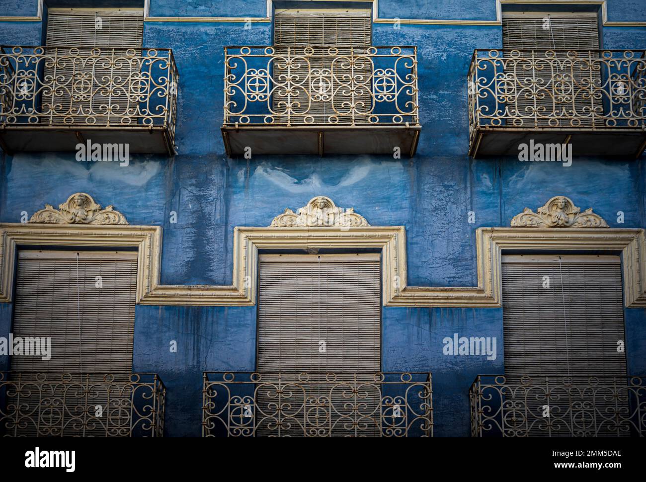 Façade de l'ancien bâtiment fenêtres bleu profond avec volets, balcons en fer forgé et moulures blanches décoratives Banque D'Images