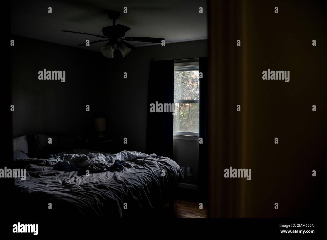 Un lit gris désordonné dans une petite chambre l'après-midi Banque D'Images