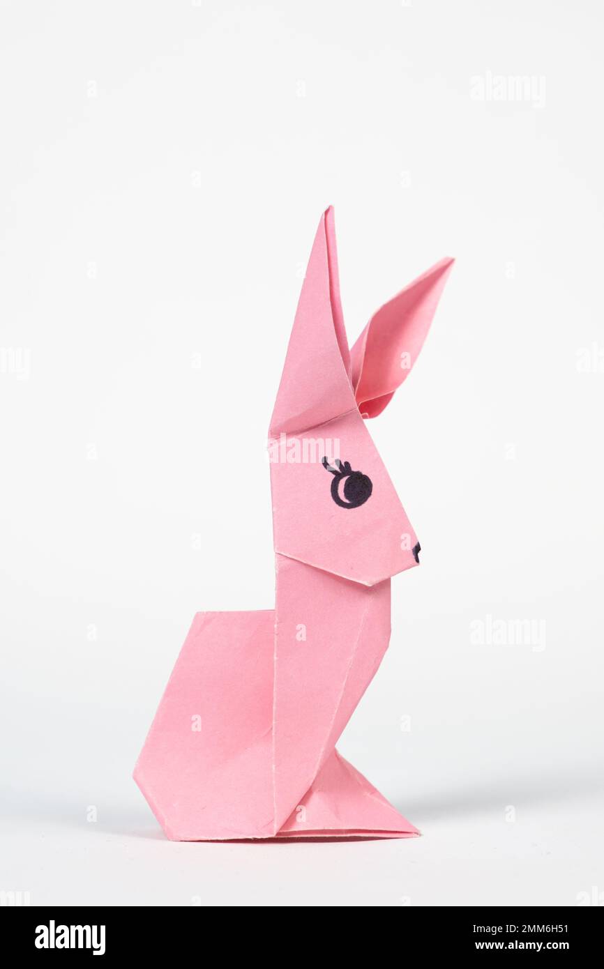 Un lapin origami rose sur fond blanc. Artisanat pour Pâques, plier à partir de papier, faites-le vous-même Banque D'Images