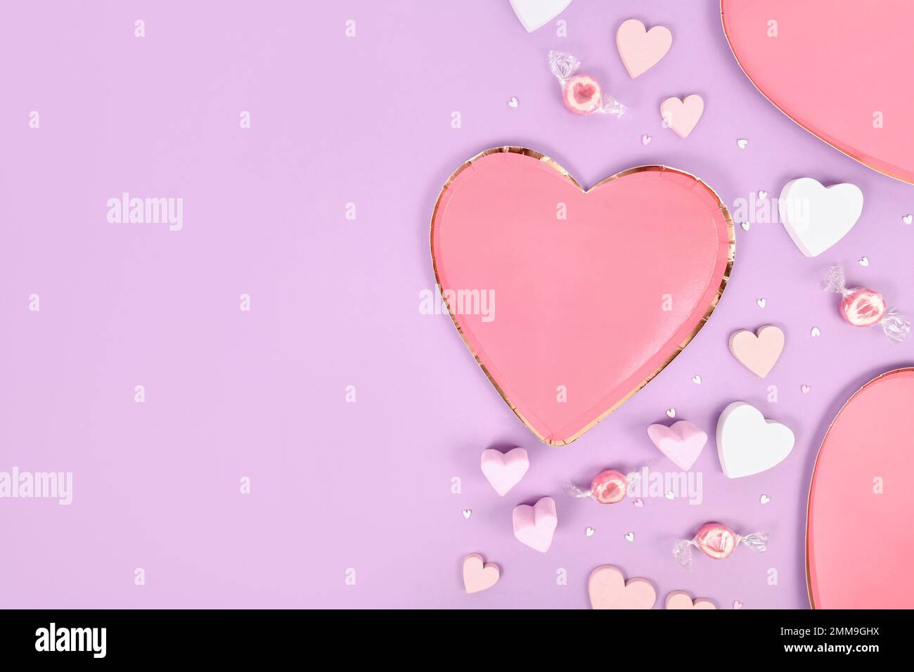 Plat couleur pastel pour la Saint-Valentin avec plaques en forme de coeur, ornements en coeur et bonbons sur fond violet Banque D'Images