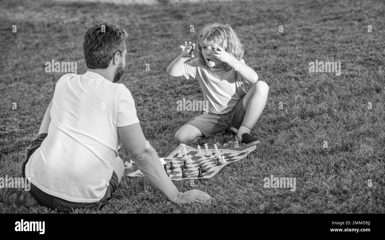 famille heureuse de père homme et fils enfant jouant aux échecs sur l'herbe verte dans le parc en plein air, éducation Banque D'Images