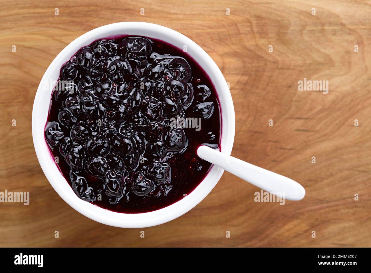 Confiture maison fraîche faite de baies de Calafate de Patagonie (lat. Berberis heterophylla) servie dans un bol blanc, photographiée au-dessus du bois Banque D'Images