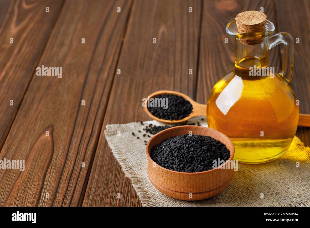 huile de cumin noire en bouteille de verre et graines dans un bol et dans une cuillère sur une table Banque D'Images