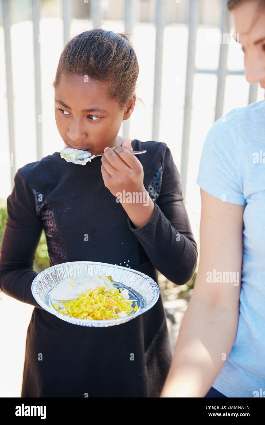 Elle n'a plus l'air affamée. une jeune fille se fait nourrir à une aide alimentaire. Banque D'Images