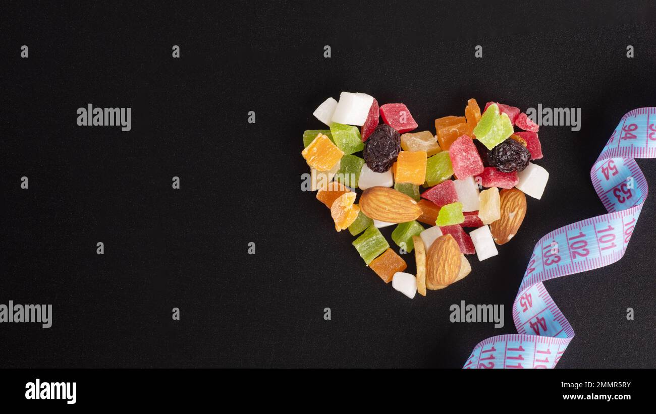 Concept alimentaire pour la Saint-Valentin. Concept amincissant. Fruits secs et noix en forme de coeur et ruban de mesure isolé sur fond noir, copie de spac Banque D'Images