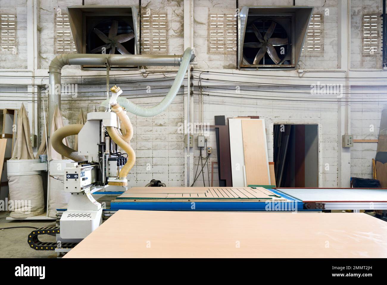 Table de travail entièrement chargée de contreplaqué dans une usine industrielle produisant des pièces de meubles en bois. Un ventilateur d'extraction est installé sur un mur de briques en béton léger Banque D'Images