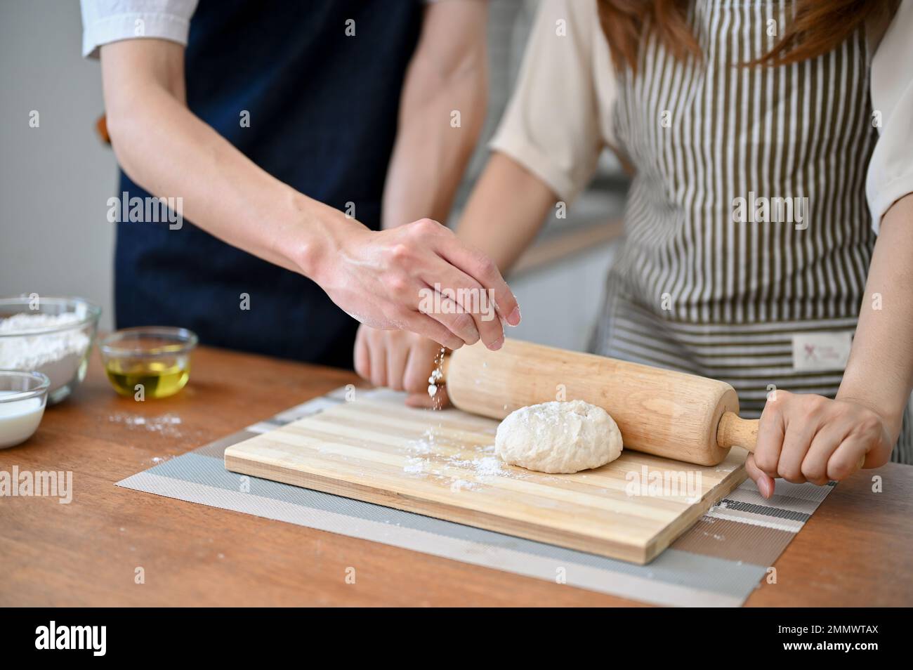 Coupe courte d'un couple adorable qui fait de la pâte ensemble dans la cuisine, pétrissage de la pâte brute avec une broche à roulettes. Banque D'Images