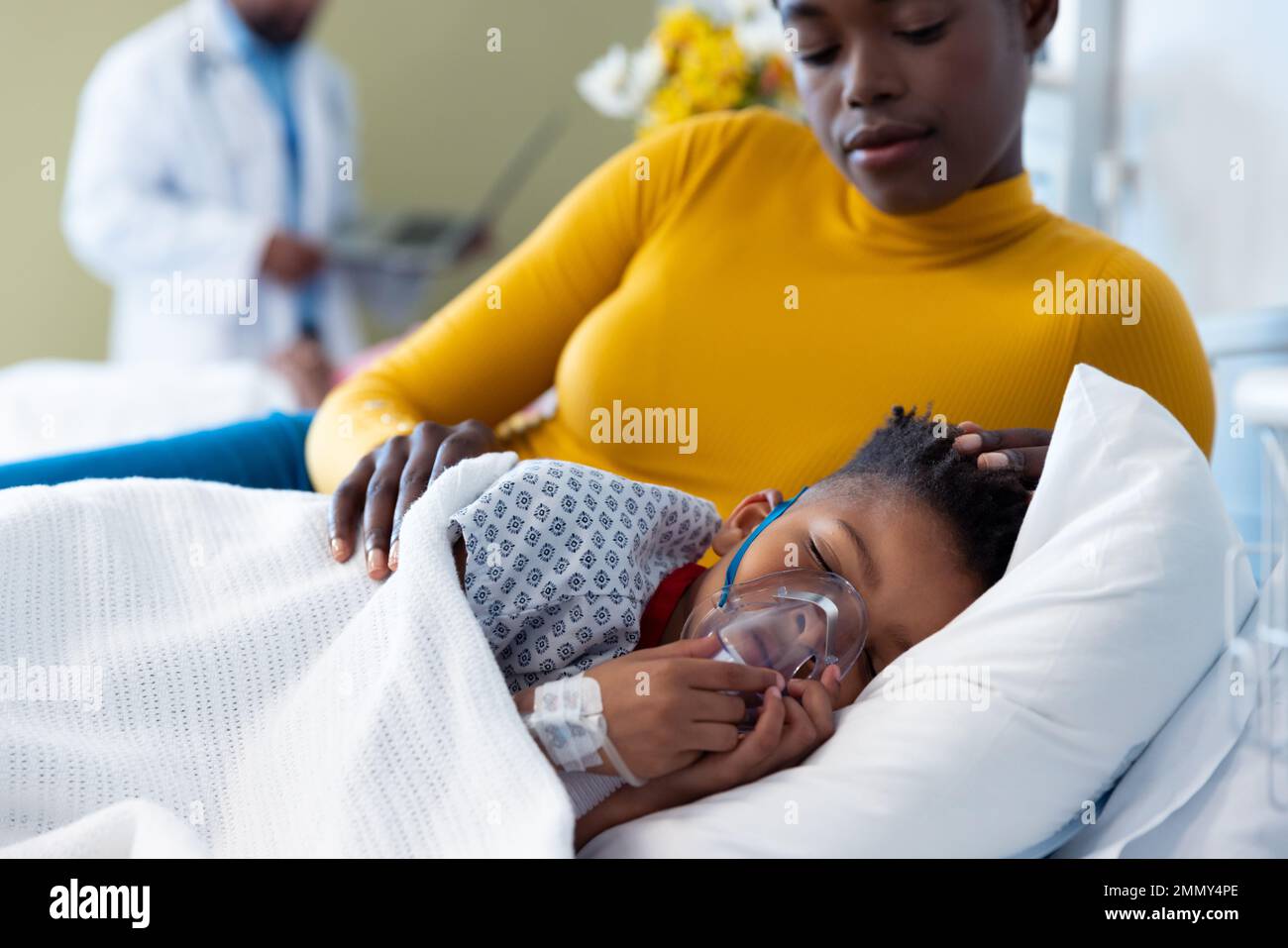 Mère afro-américaine à côté de son patient sous ventilateur endormi dans le lit d'hôpital Banque D'Images