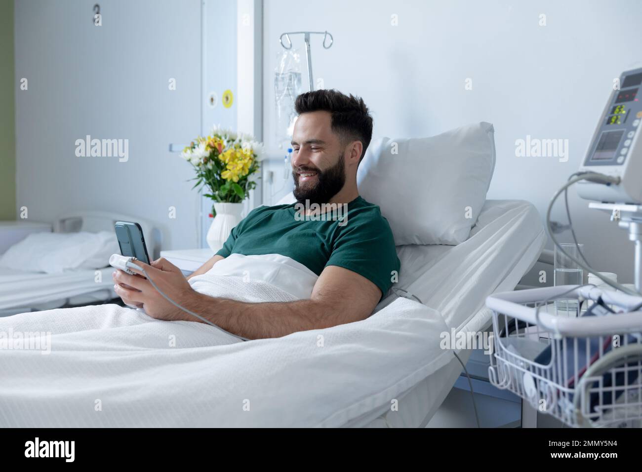Patient mâle caucasien allongé dans le lit et utilisant un smartphone à l'hôpital Banque D'Images