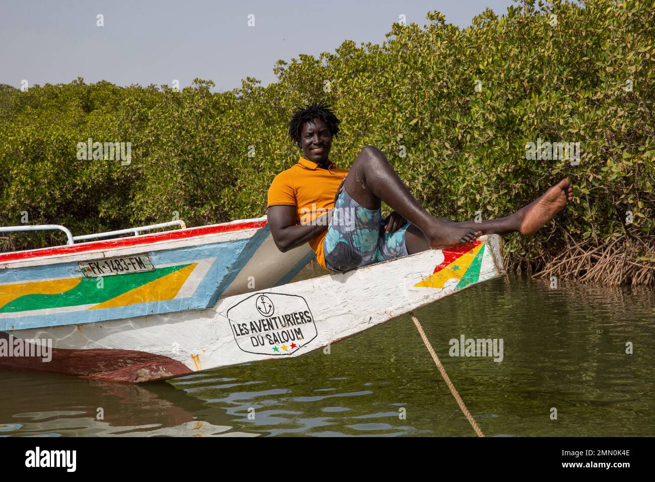 Sénégal, delta de Saloum classé au patrimoine mondial par l'UNESCO, Pierre Diouf, créateur de l'agence touristique Aventuriers du Saloum, situé devant un canoë multicolore flottant au milieu de la mangrove Banque D'Images
