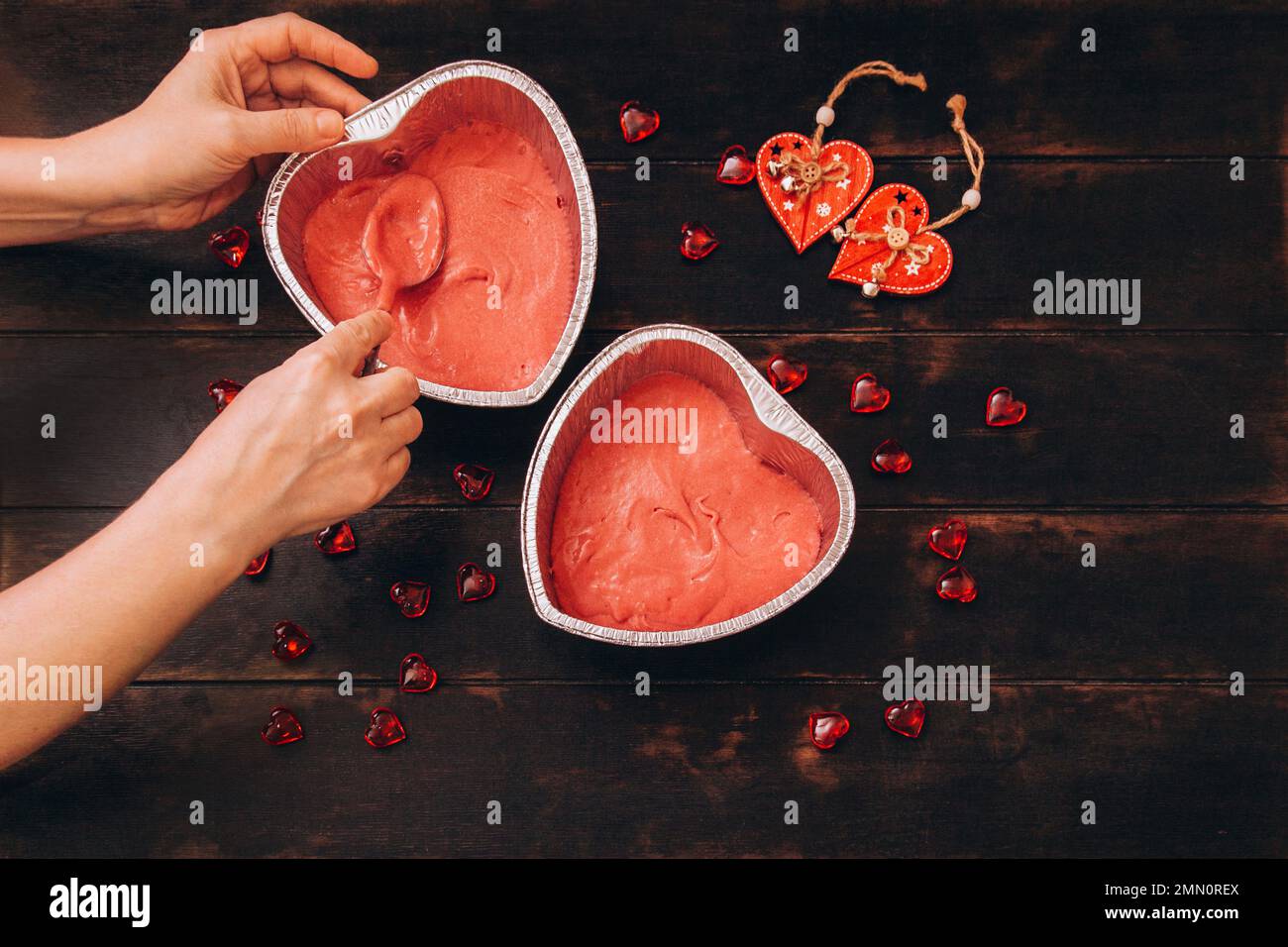 Les mains des femmes avec une cuillère mettre la pâte sous forme de papier d'aluminium pour cuire un gâteau sous forme de coeur. Préparation pour la Saint-Valentin. Banque D'Images