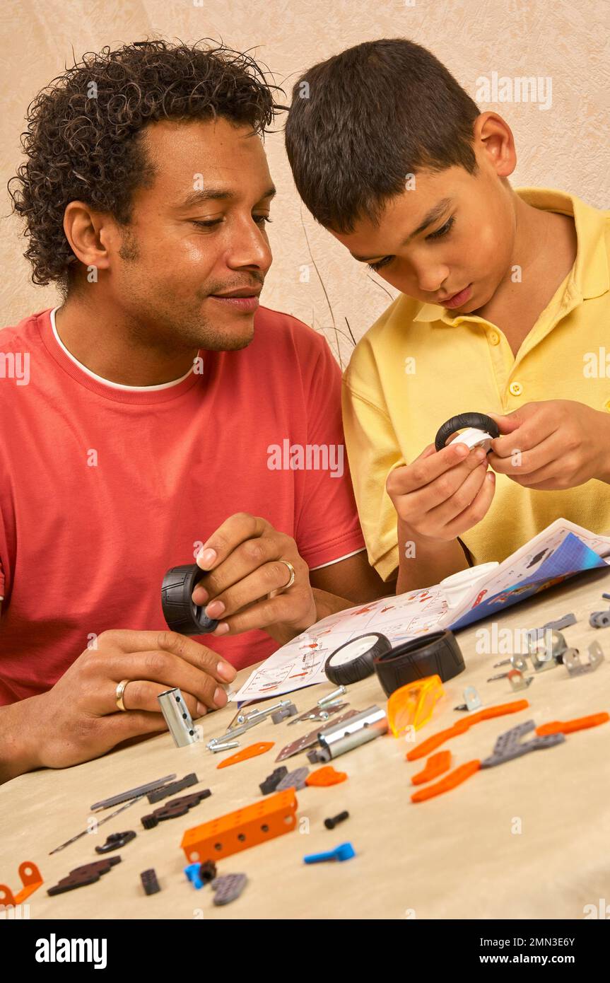 Un jeune garçon et un homme adulte vérifient les instructions et assemblent ensemble un kit de voiture jouet en métal et en plastique Banque D'Images