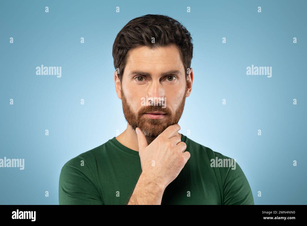 Portrait d'un beau homme caucasien barbu posé sur fond bleu et touchant le menton Banque D'Images