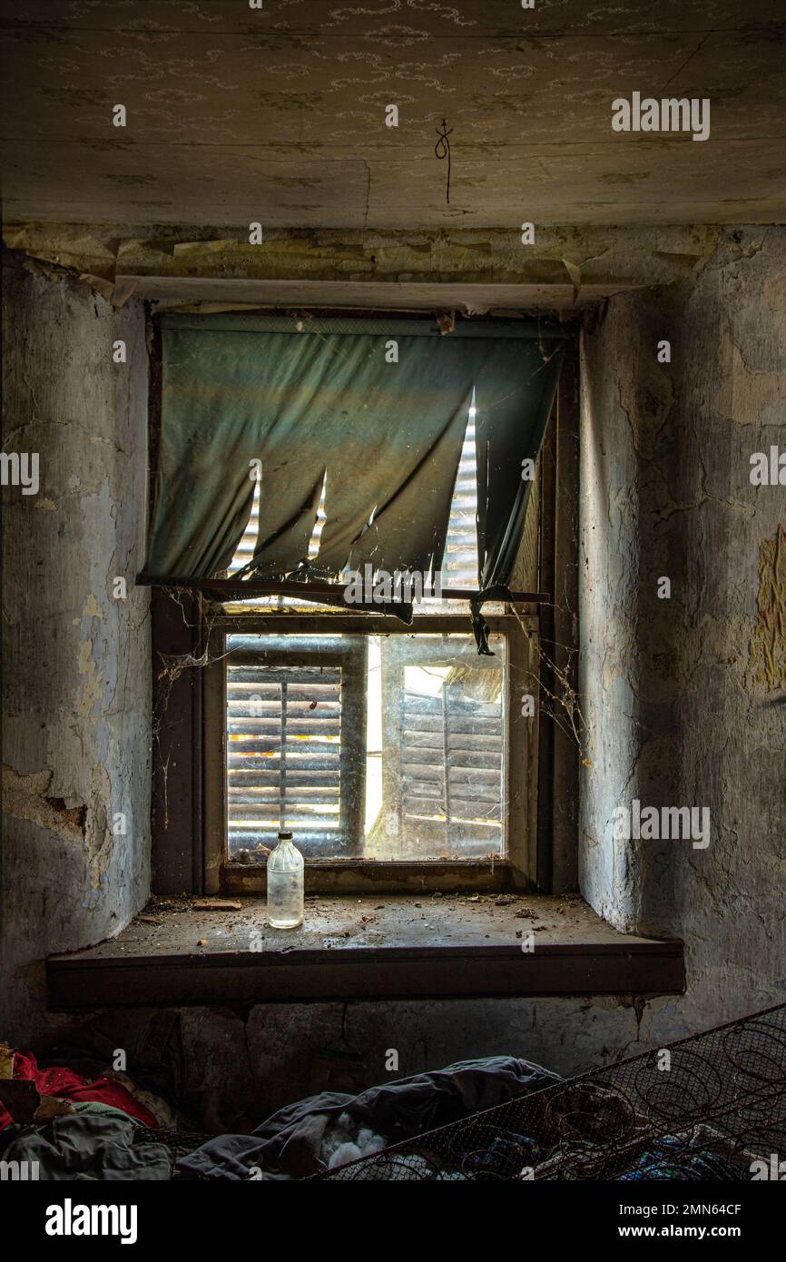 Fenêtre cassée, rideaux déchirés et bouteille sale dans l'intérieur de maison abandonnée, Pennsylvanie USA Banque D'Images