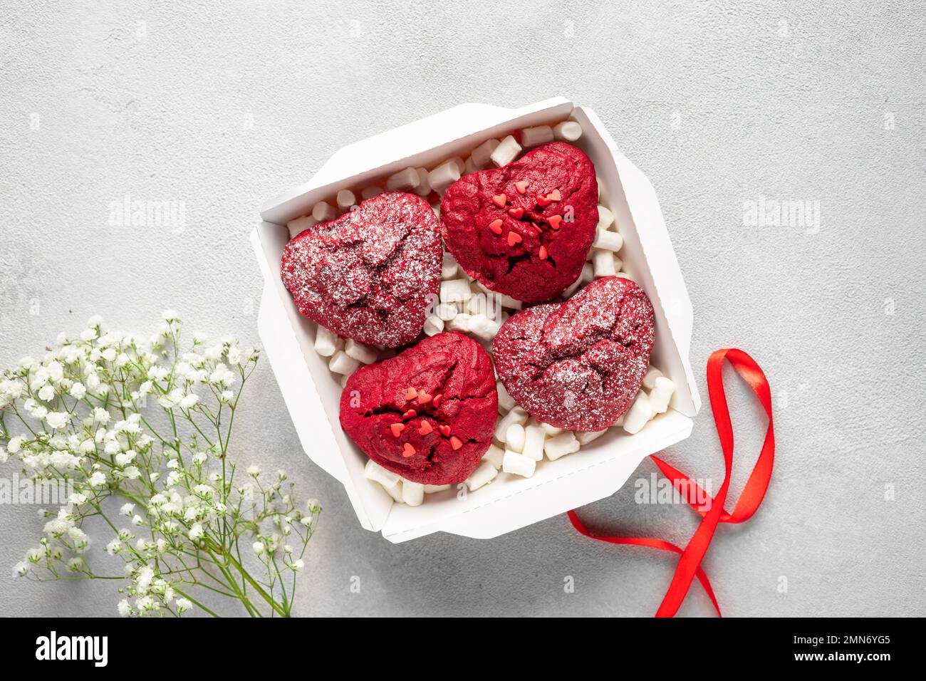 Ensemble de petits gâteaux en velours rouge dans une boîte en papier avec guimauves, fleurs et ruban Banque D'Images