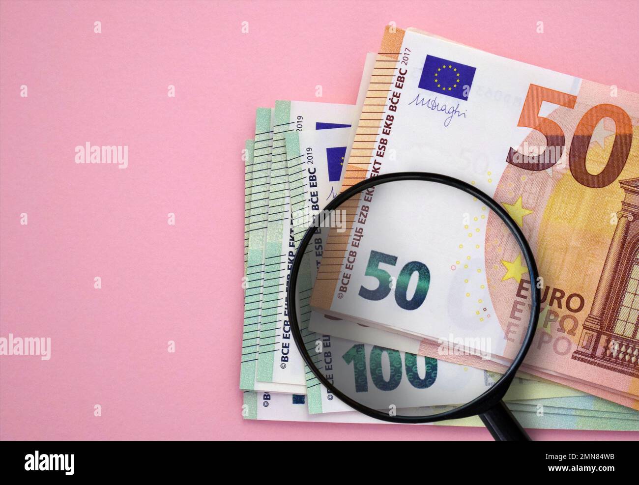 Paquet de billets en euros (50 euros, 100 euros) et loupe sur fond rose. Monnaie européenne, épargne, richesse Banque D'Images