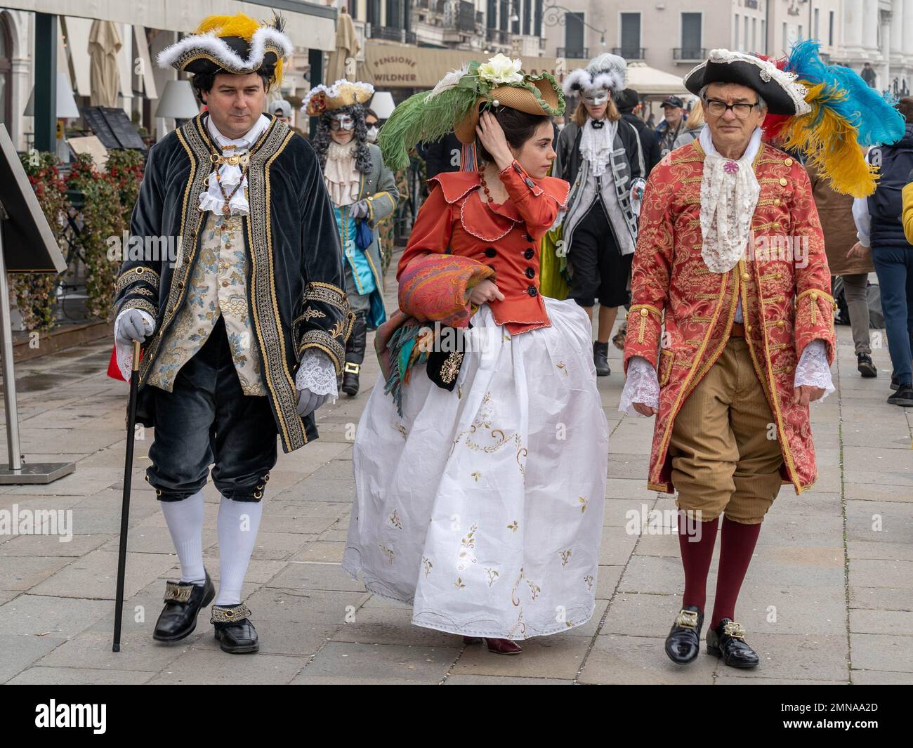 Deux hommes plus âgés suivent une jeune femme, tous vêtus de robes de carnaval, au Carnaval de Venise Banque D'Images