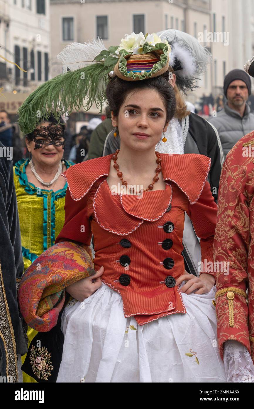 Jolie jeune femme vêtue de robe de carnaval : manteau rouge, jupe blanche et petit chapeau avec de grandes plumes pose au carnaval de Venise Banque D'Images