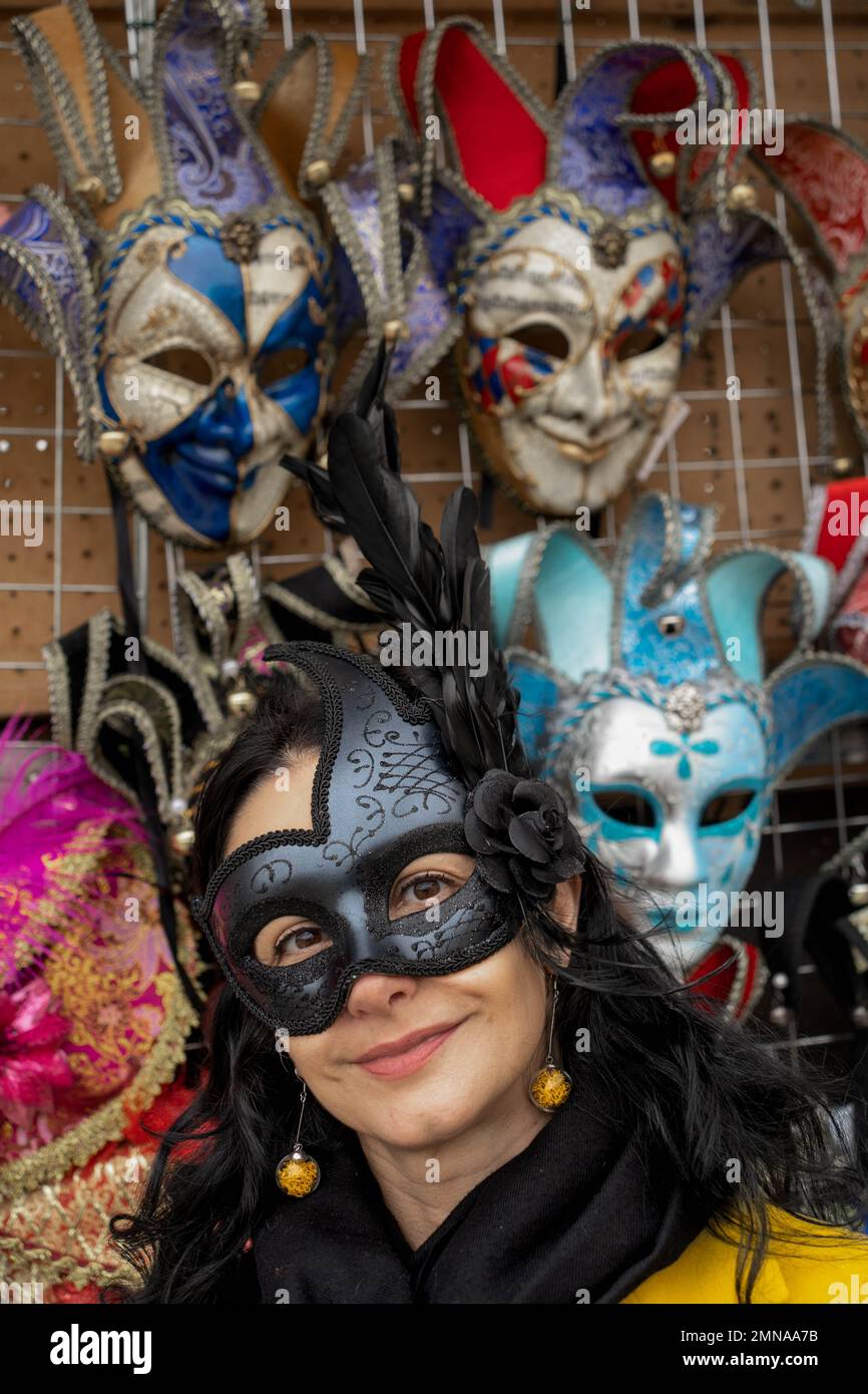 Une femme d'âge moyen portant un masque noir avec les plumes posant avec les masques affiche le fond au carnaval à Venise, Italie Banque D'Images