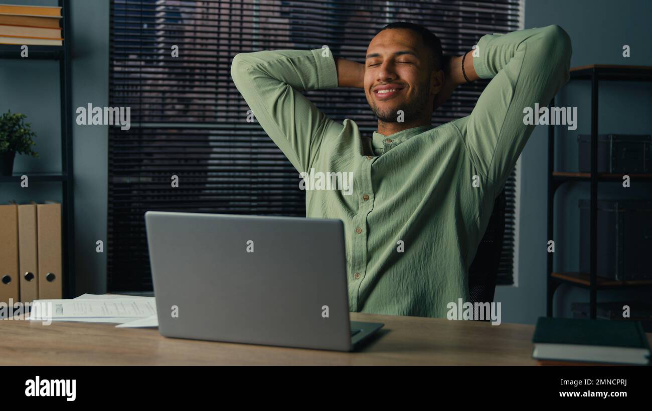 Un homme d'amérique latine heureux a terminé son travail sur un ordinateur portable un jeune homme d'affaires satisfait s'est assis au bureau avec les mains derrière la tête se sentant soulagé après le travail Banque D'Images