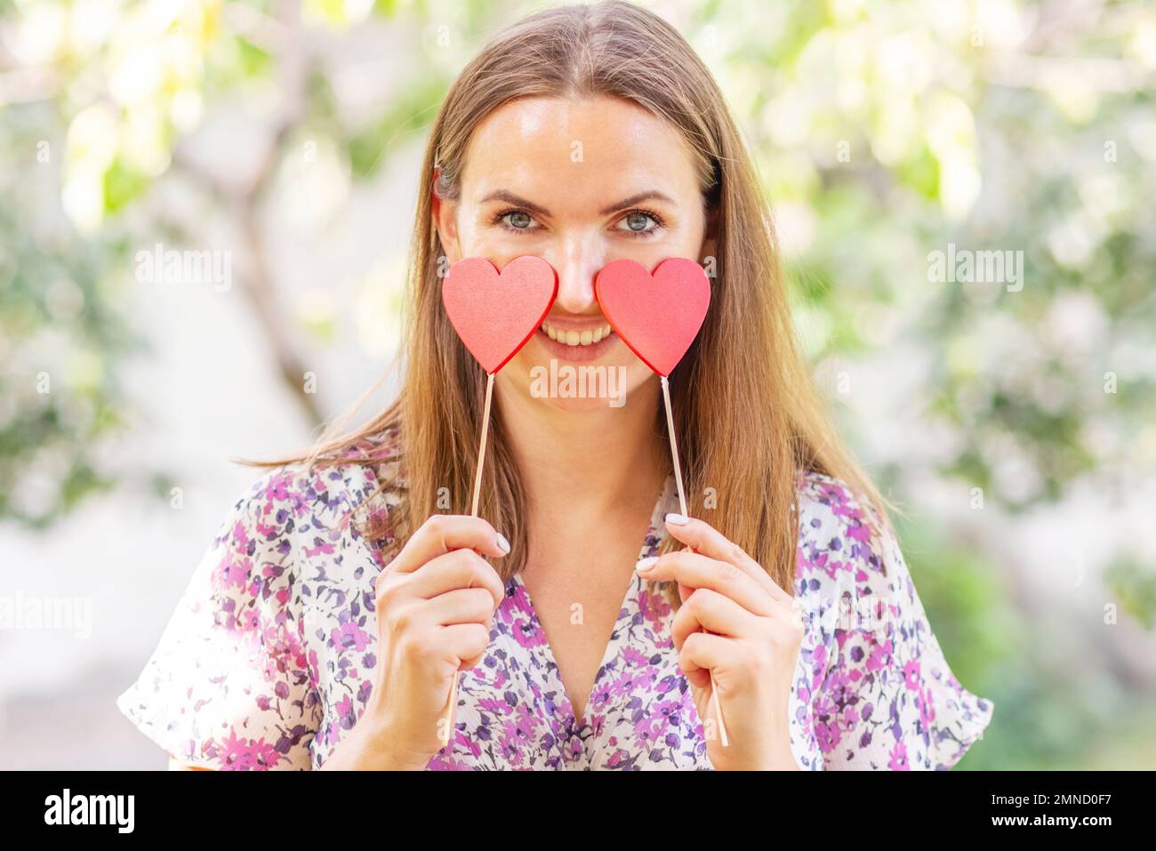 Femme avec deux coeurs décoratifs dans ses mains souriant sur fond naturel Banque D'Images