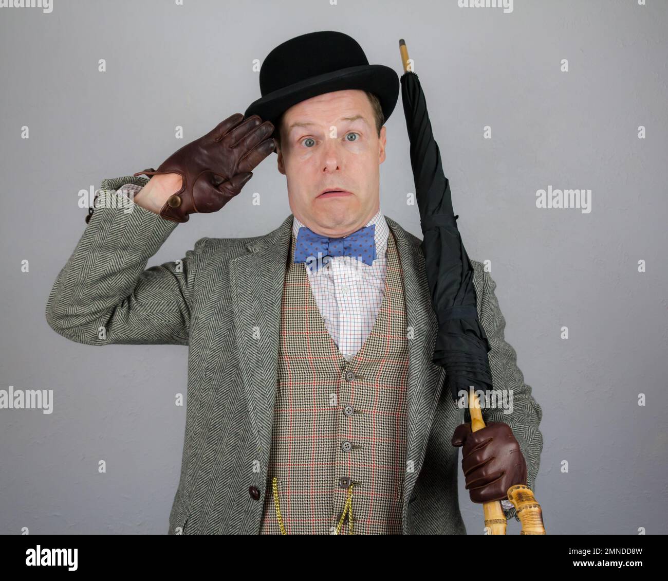 Portrait du personnage britannique en costume en tweed et chapeau de bowling tenant un parapluie comme un fusil et saluant avec audace. Concept de l'acteur Vintage Vaudeville Banque D'Images